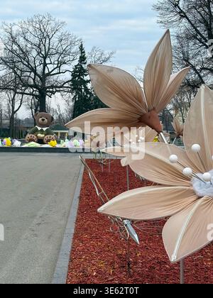A charming outdoor spring installation featuring large beige fabric flowers in the foreground and a cute teddy bear sculpture in the background. Stock Photo