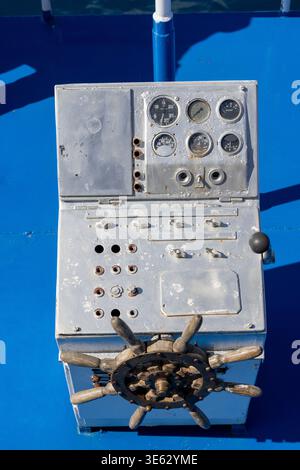 Control panel features a steering wheel, gauges, switches, and knobs on a bright blue ship deck. Sunny outdoor setting creates a functional nautical a Stock Photo
