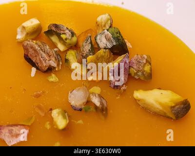 Close-up photograph of creamy orange soup, likely pumpkin or butternut squash, garnished with roughly chopped pistachio nuts. The smooth, vibrant Stock Photo