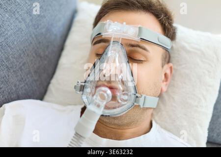 Man using CPAP mask for obstructive sleep apnea treatment on bed at home Stock Photo