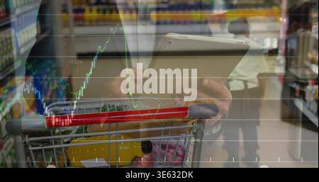 Holding tablet, Asian man scanning prices in store aisle with cart, yellow bottle, chart overlay Stock Photo