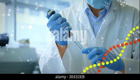 Pipetting tech in surgical mask and blue gloves transferring liquid at bench with pipette and tube Stock Photo