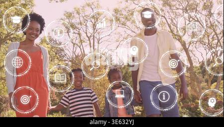 Family of four walking hand-in-hand in park, causing HUD icons floating around family, showing book Stock Photo