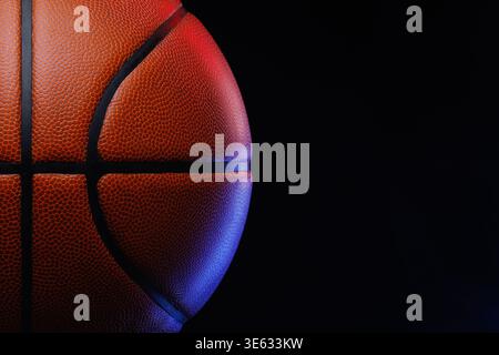 Basketball ball resting against dark background with vibrant red and blue studio lighting Stock Photo