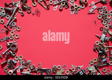 Assorted screws nuts and bolts forming frame on red background with copy space in center Stock Photo