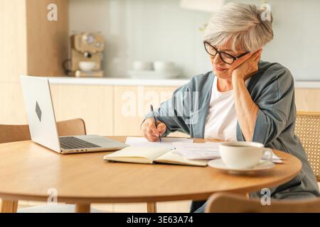 Online education courses webinar concept. Middle aged senior woman using laptop computer writing notes. Focused mature old woman enjoying studying online from home written records doing online work Stock Photo