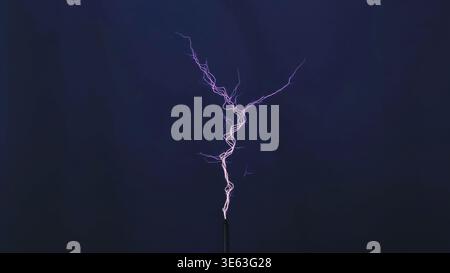 Electrical discharge creating a purple plasma arc from a Tesla coil during experiment Stock Photo