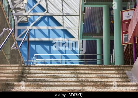 A modern interior staircase featuring granite steps with glass and metal railings leads upward toward a vibrant blue wall. Geometric shadows from Stock Photo