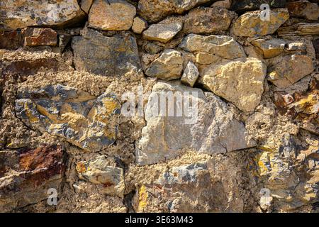 Rugged stone wall texture with uneven, weathered rocks. Natural sunlight highlights rough surfaces and earthy tones. Ideal for backgrounds, constructi Stock Photo