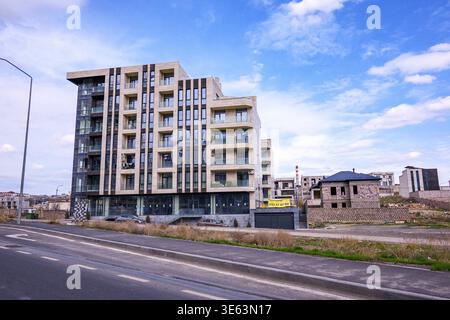 Modern apartment building stands tall against bright blue sky with scattered clouds. Concrete facade features large glass windows and balconies. Empty Stock Photo