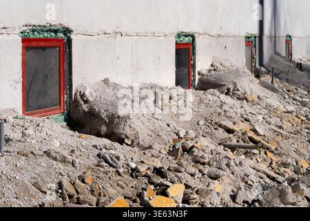 A large pile of construction debris consisting of broken bricks and concrete pieces against a wall with four red windows. Stock Photo