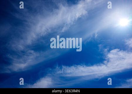 Sun shines brightly through wispy clouds in deep blue sky. Sky appears calm and peaceful, perfect for serene backgrounds. Ideal for travel, nature, or Stock Photo
