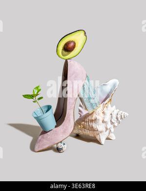 High heel shoe features an avocado, a small plant in a pot, and a seashell, creating a unique artistic composition with vibrant elements Stock Photo