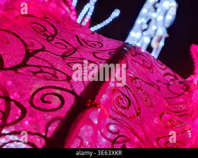 Close-up macro photograph of vibrant magenta or hot pink fabric featuring intricate dark red or black swirling filigree patterns. The textile appears Stock Photo