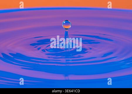 A drop of water falls and bounces in a blue and orange-hued body of water Stock Photo