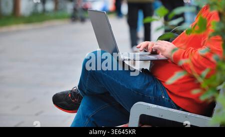 Person working remotely outdoors on laptop, typing on keyboard in urban park Stock Photo