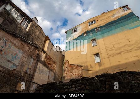 Looking up at weathered yellow and teal painted building facades rising above crumbling brick walls under a dramatic cloudy sky in Istanbul Stock Photo