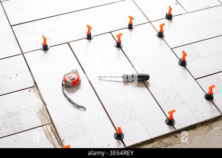 Process of floor tile installation, leveling system, precise placement, renovation work, tools for laying ceramic tiles, home improvement project. Stock Photo
