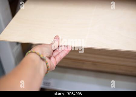 Hand of a woman holding a light wooden board or laminate sample in a hardware store. Building materials, home renovation, construction shop, professio Stock Photo