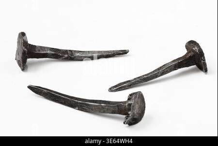 Three old iron nails rest on a clean white background, revealing intricate designs and historical significance. Their weathered surfaces tell stories Stock Photo