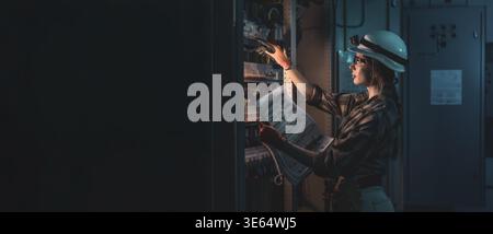 Female electrician inspecting electrical switchboard using technical blueprint. Industrial energy. Stock Photo