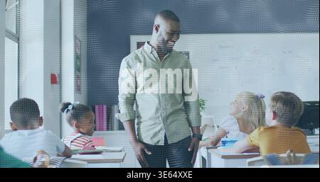 Teaching teacher in green shirt, leaning between desks in school class, engaging kids using notes Stock Photo