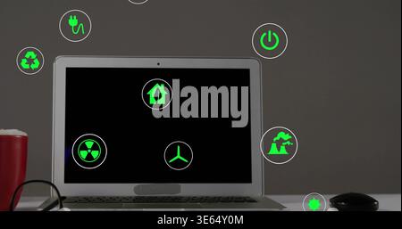 Displaying open silver laptop showing green energy icons on light desk, with red cup and glasses Stock Photo