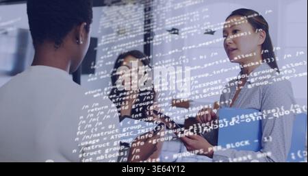 Discussing three women in business-casual office, holding tablet, blue folder, showing code overlay Stock Photo
