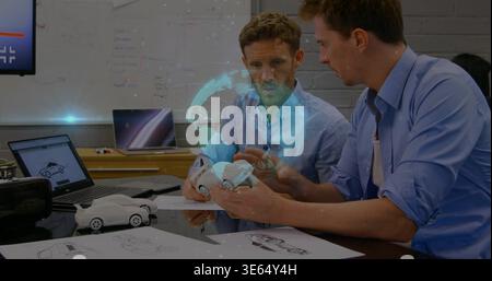 Holding white scale car, two designers wearing blue shirts examining model in studio with AR globe Stock Photo