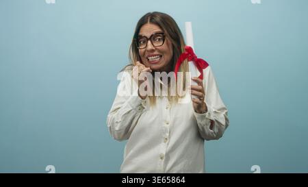 Middle aged woman holding a diploma with red ribbon and biting her fingernail in studio; nervous anticipation. Stock Photo