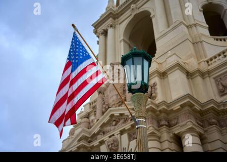 American flag waving in front of the historic Pasadena City Hall. Close-up of US flag and vintage street lamp against Mediterranean Revival architectu Stock Photo