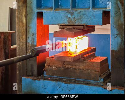 Professional bladesmith forging damascus steel using a powerful hydraulic press in a workshop. Stock Photo