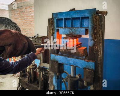 Professional blacksmith forging damascus steel using a powerful hydraulic press in a workshop. Stock Photo