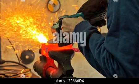Artisan blacksmith grinding red-hot steel with an angle grinder in a shower of sparks. Stock Photo