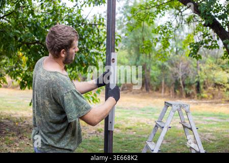 Man checking the vertical alignment of a metal post with a bubble level in a garden. Construction precision, measurement tool, professional building. Stock Photo