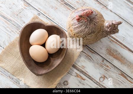 Fresh Brown Eggs in Wooden Bowl with Hen on Rustic White Wood Overhead View Stock Photo