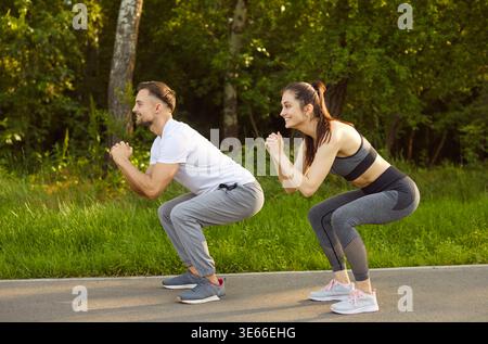 Sporty couple doing squat in green outdoor park, fit man and woman squatting, exercising together Stock Photo