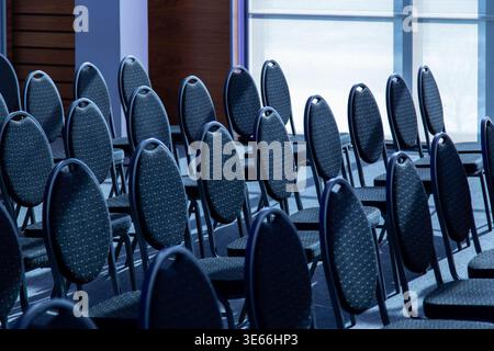 Rows of empty chairs fill an indoor event room prepared for a meeting or presentation. The seating layout forms a repeated pattern Stock Photo