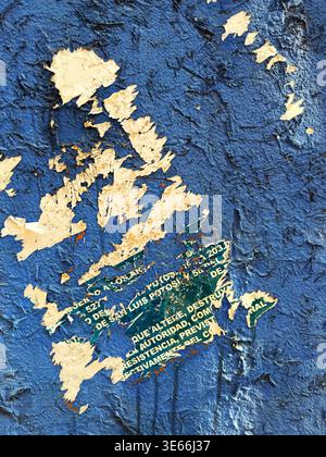 Close up view of a rough blue painted wall with torn paper posters revealing layered textures Stock Photo