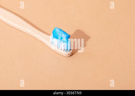 Bamboo toothbrush with blue toothpaste on beige background, eco friendly oral care concept. Top view, copy space. Stock Photo