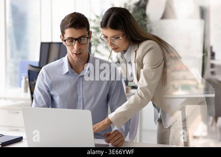 Woman assisting to male colleague seated in front of laptop Stock Photo