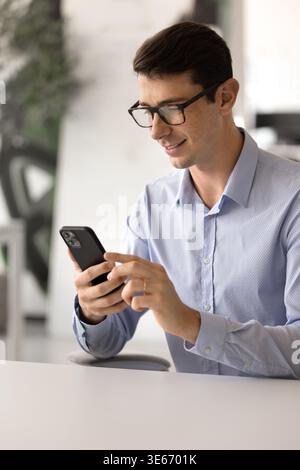 Young Spaniard man in casual shirt using smartphone at workplace Stock Photo