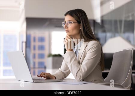 Woman thinking while working at laptop in office Stock Photo