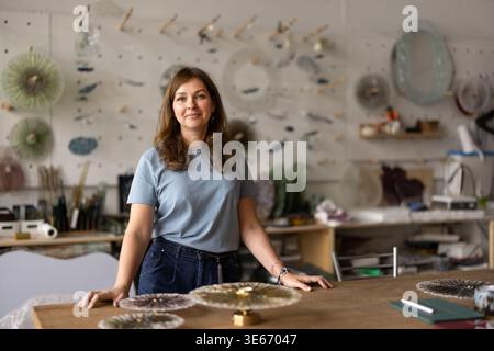 Portrait of smiling female artisan standing at workshop table Stock Photo