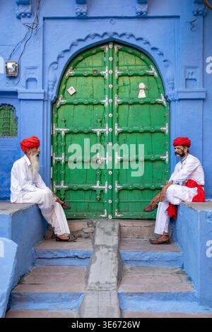 Two Rajasthani men wearing traditional white kurta and red turbans,  talking in the Blue City of Jodhpur, India Stock Photo