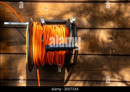 Wall mounted extension cord reel on wooden exterior wall, outdoor power supply detail. Concept: outdoor electricity access Stock Photo