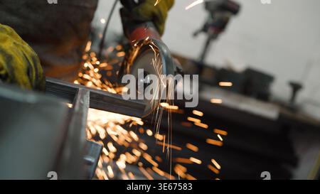 Metal worker cutting metal bar using angle grinder, producing bright sparks in industrial workshop Stock Photo