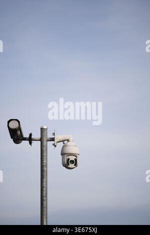 Security camera on a pole with a light fixture nearby Stock Photo