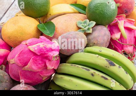 Assorted tropical fruits including dragon fruit mango lime and bananas on rustic surface Stock Photo