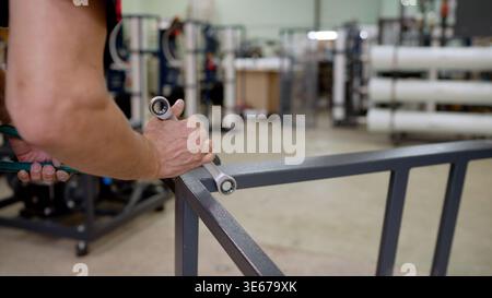 Close up of a male worker hands using a wrench. A mechanic assembles a gray metal structure in a factory workshop. Shallow depth of field blurs the in Stock Photo